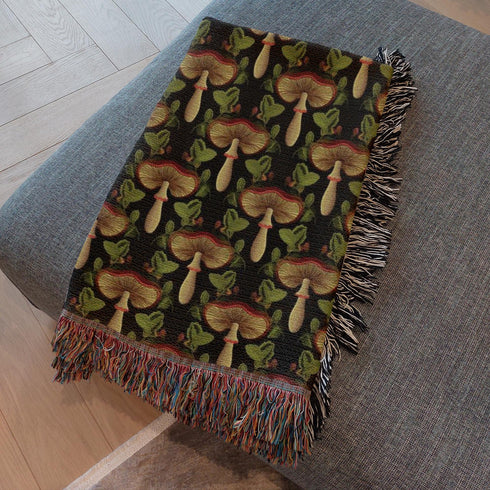 generatedA woven cotton throw featuring an intricate mushroom and foliage pattern in deep charcoal and golden hues, framed by soft fringe.-preview-2